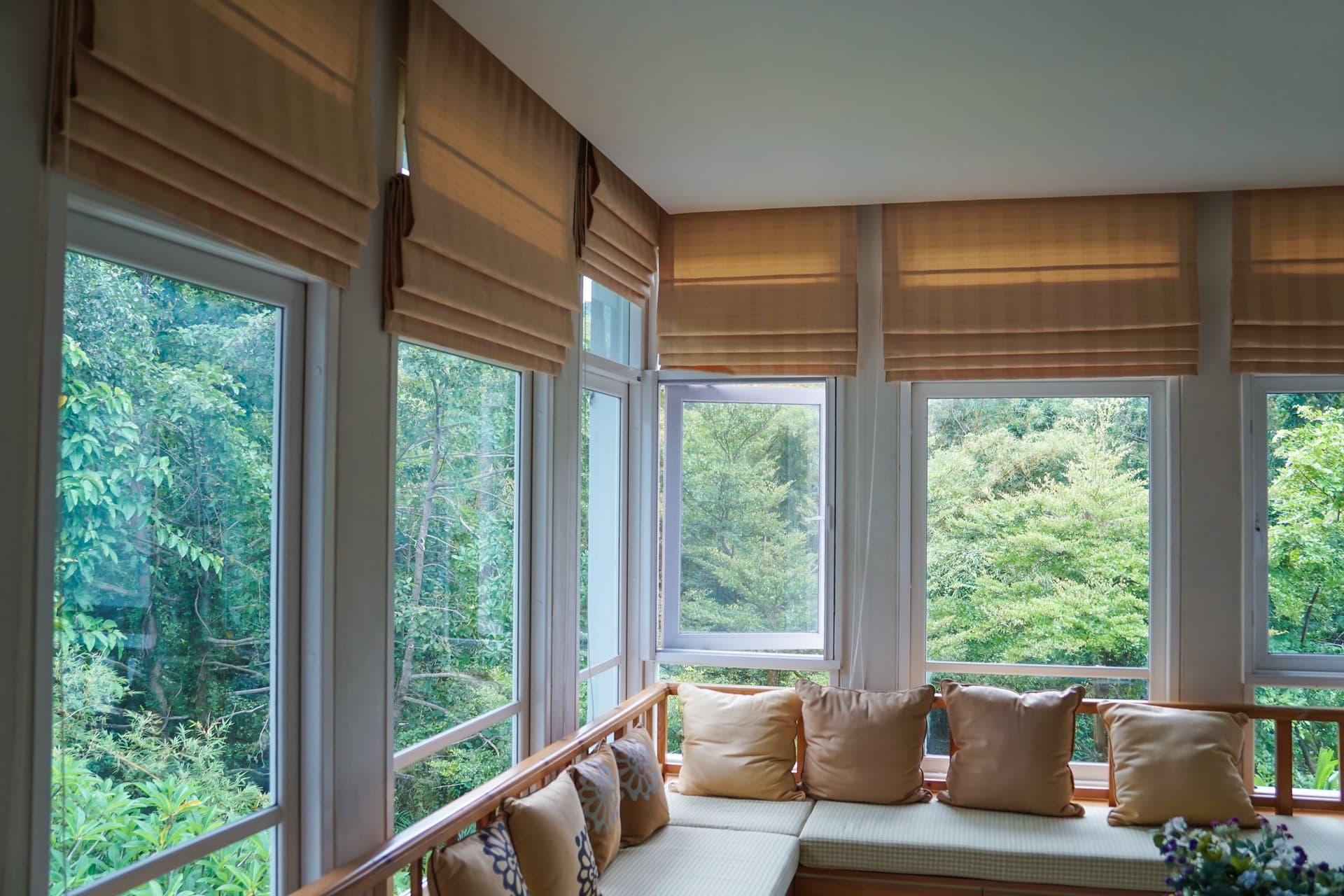 Sunroom with casement windows roman shades and built-in window seat overlooking trees