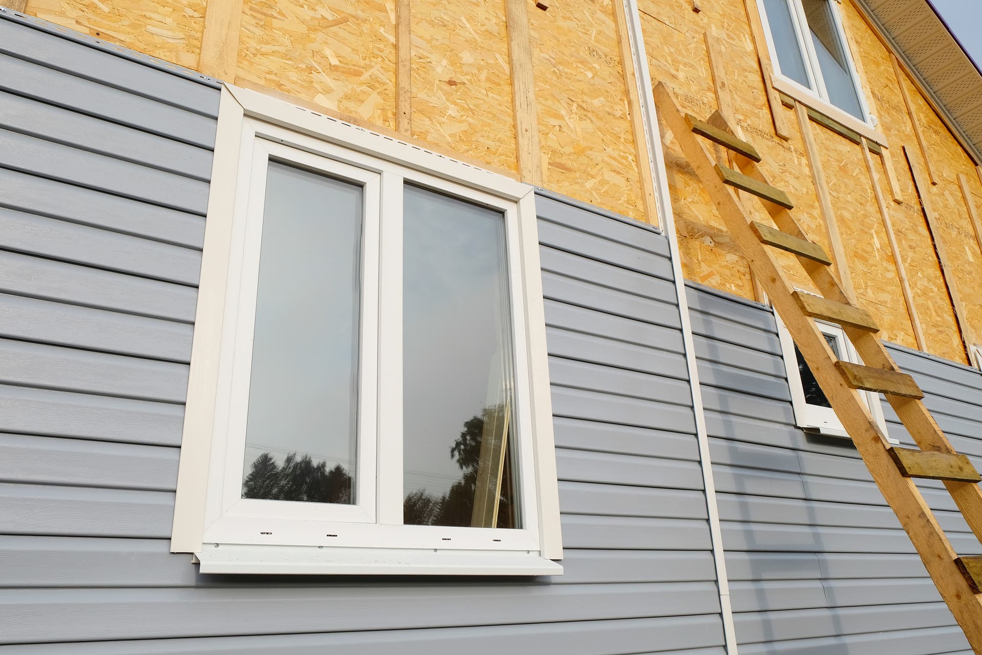 Gray vinyl siding installation in progress on a residential home with window trim detail