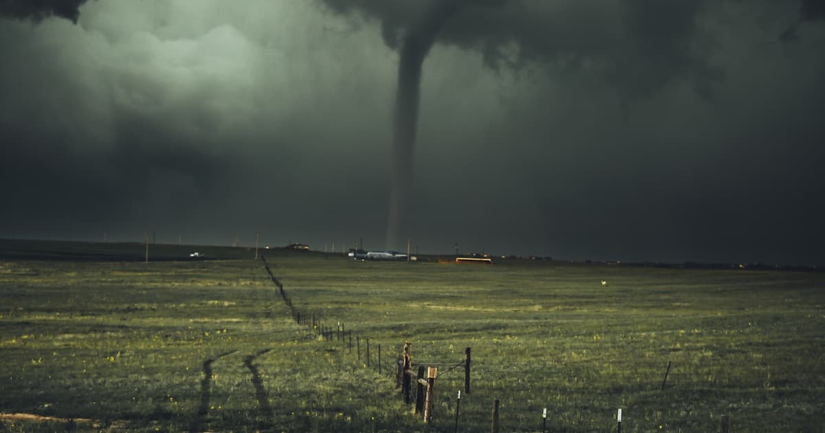 Large tornado touching down over open Colorado plains during severe storm season, dark storm clouds above a rural fence line