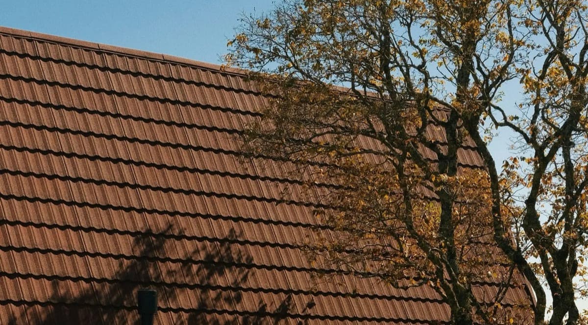 Brown stone-coated steel tile roofing close-up on a Denver, Colorado home with autumn tree in the background