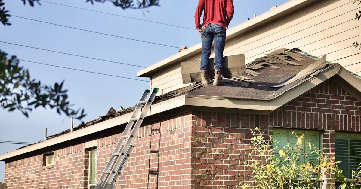 Roofing contractor standing on a damaged residential roof during tear-off and replacement on a brick home in Denver, Colorado