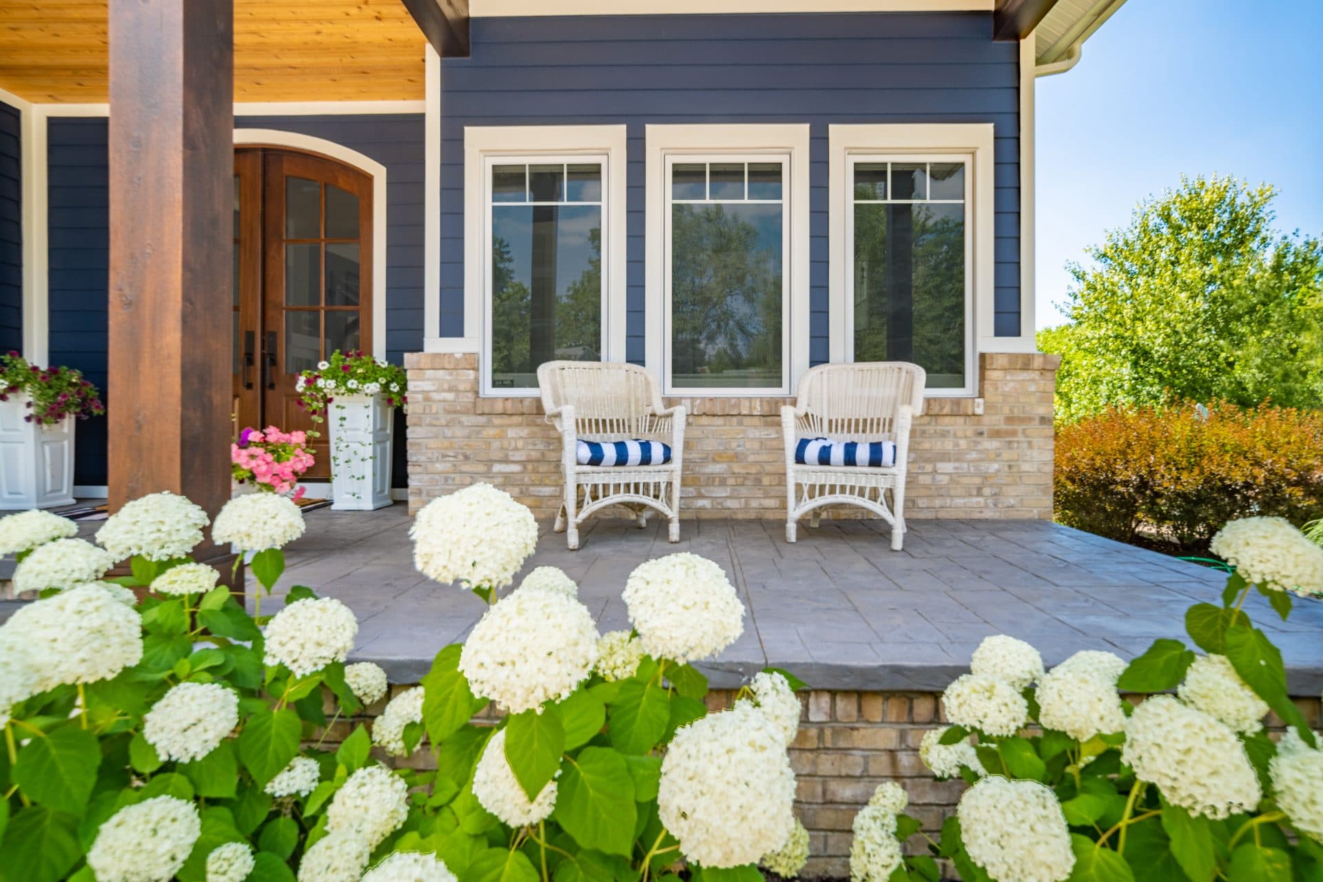Blue James Hardie lap siding with white trim on a home with chairs on the front porch and flower bushes around.
