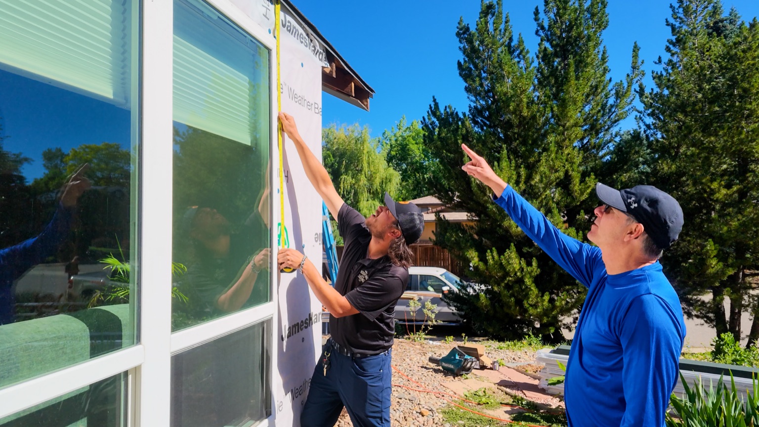 Crew member measuring James Hardie siding alignment next to a window, with Bobby observing, Boulder, CO