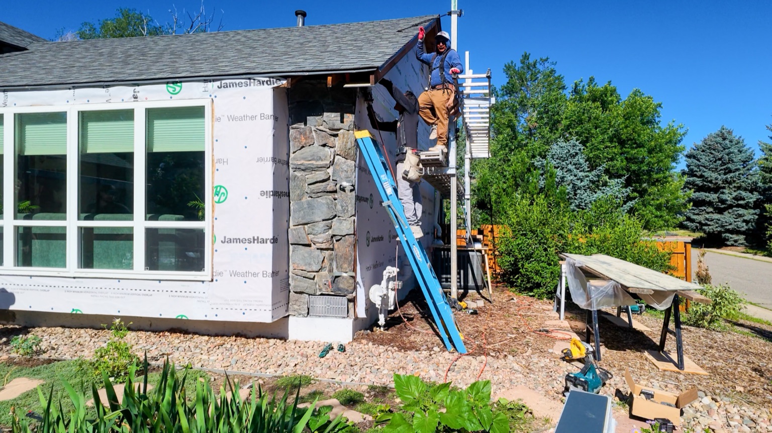 Crew installing James Hardie weather barrier on the rear of the home in Boulder, CO, with existing stone chimney visible