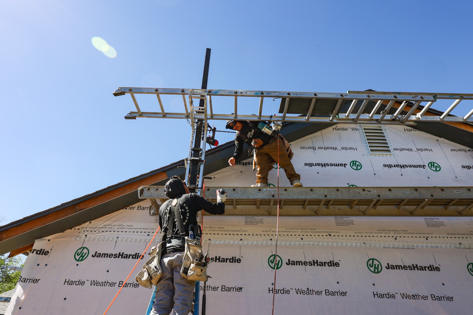 Two crew members on ladders installing James Hardie weather barrier along the roofline of a Boulder, CO home