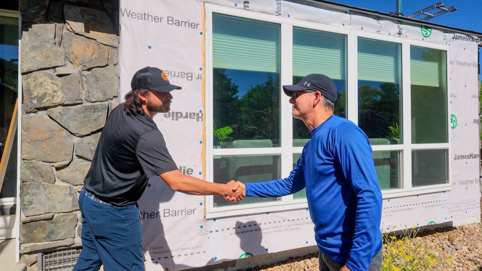 Bobby shaking hands with a Roofing & Siding Company crew member in front of the home with James Hardie weather barrier visible, Boulder, CO